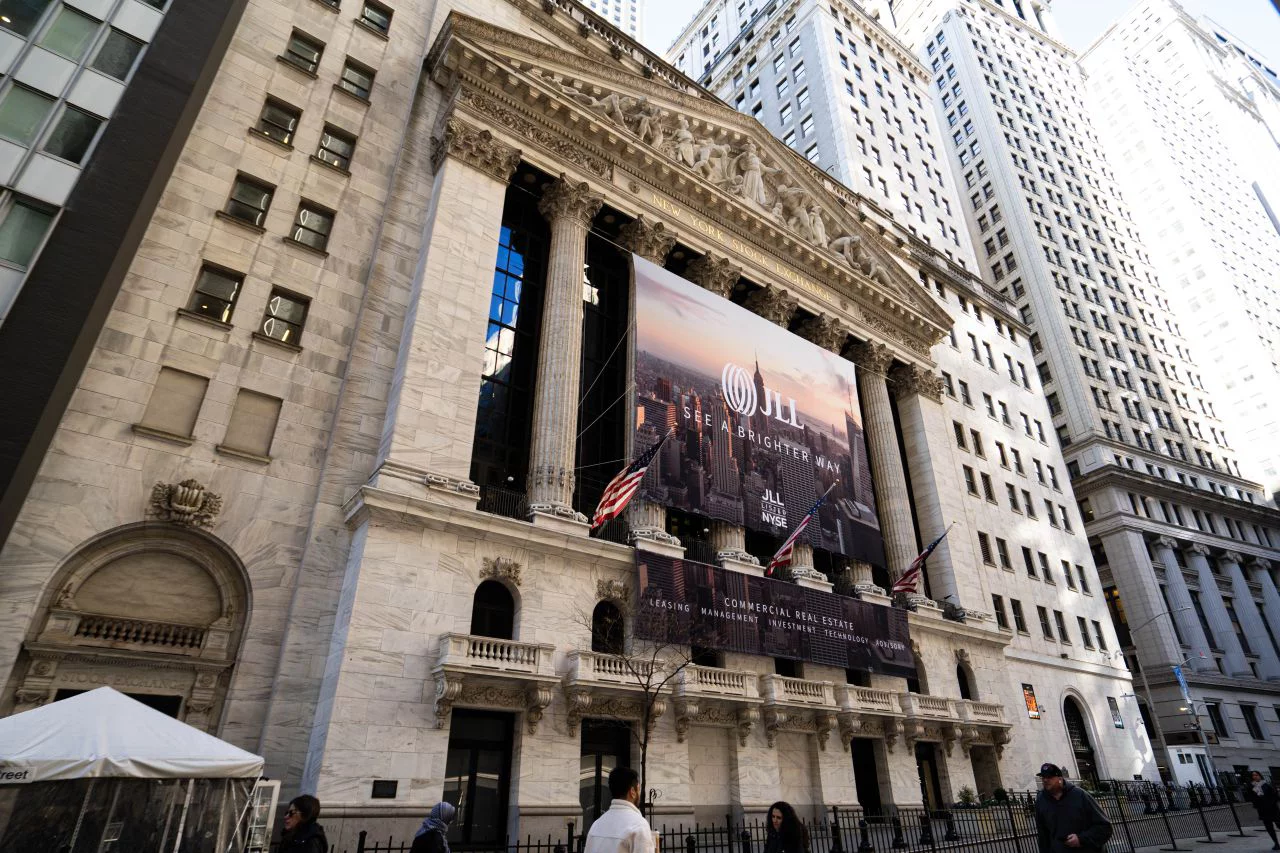 New York Stock Exchange building with JLL banner displayed on facade, surrounded by tall skyscrapers in financial district.