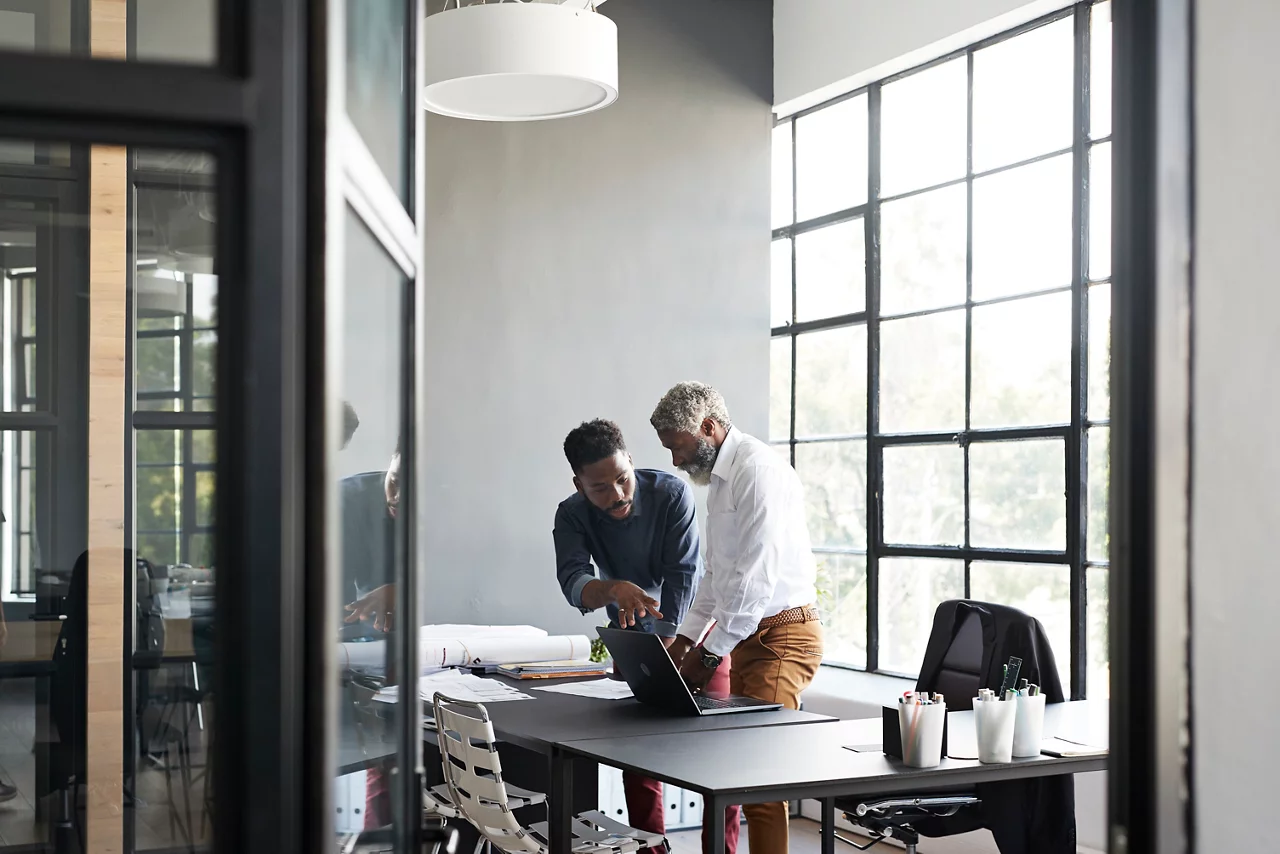 Male entrepreneurs discussing while standing by desk in modern office seen through doorway