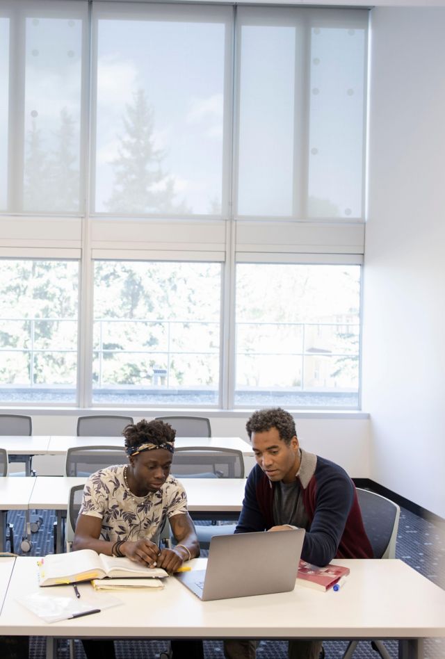 2K3A3JC Male college professor helping student at laptop in classroom